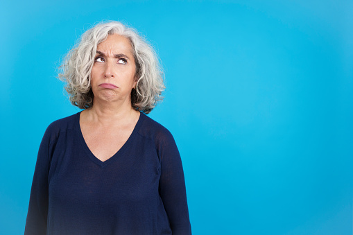 Studio portrait with blue background of an aged caucasian woman looking up with an expression of disgust