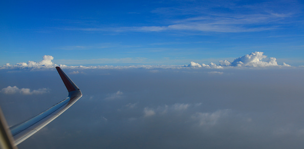 Wing of airplane over white clouds in sunny day.