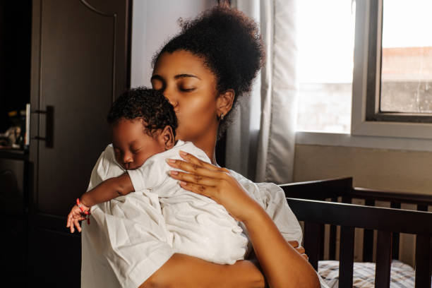 madre adulta joven sosteniendo y besando a su recién nacido. - afrocaribeño fotografías e imágenes de stock