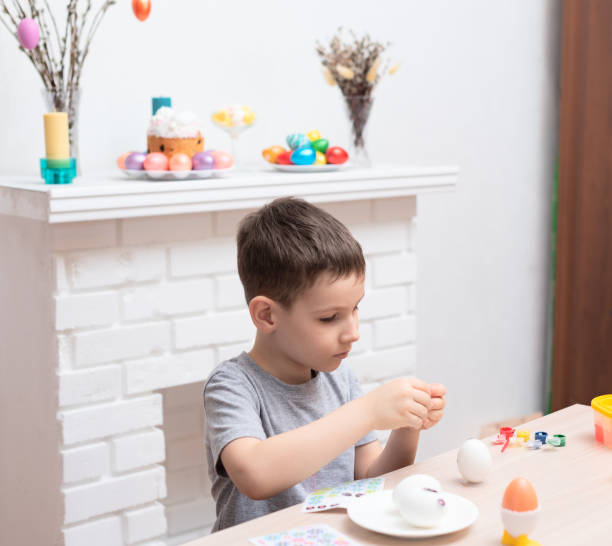 istock Child boy decorating and painting easter eggs against defocused fireplace with Easter decorations on it. Selective focus. Happy Easter concept. Process of crafting at home 1471570463