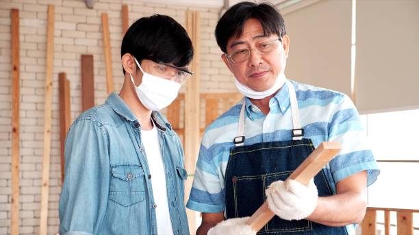 Asian senior carpenter teaching apprentice while working together in joinery workshop. The operational planning meeting. DIY maker and carpentry work
