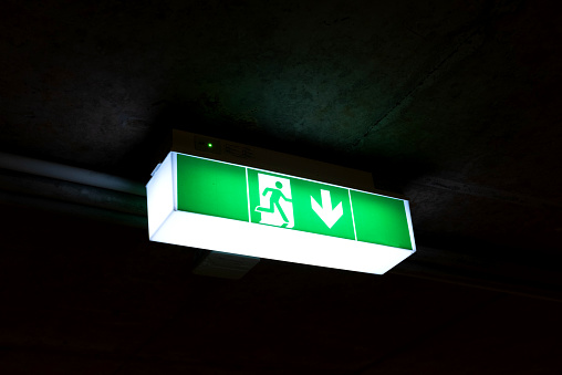 Stock photo showing close-up view of a wall mounted. illuminated emergency fire exit sign.