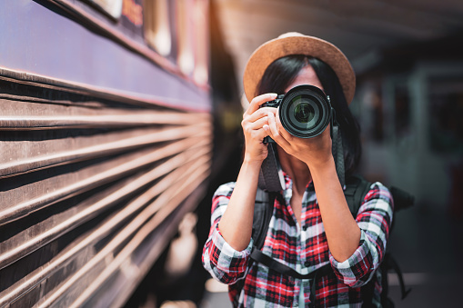 Tourist woman taking a photo with camera of side of train on railway background. Young asian woman traveler with backpack in the railway, Travel concept