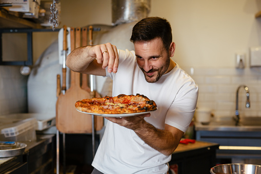 Male chef is sprinkling fresh oregano over a traditionally made home pizza.