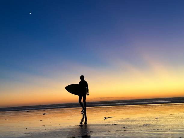 istock Sun rays over surfer and a quarter at sunset. 1471579676