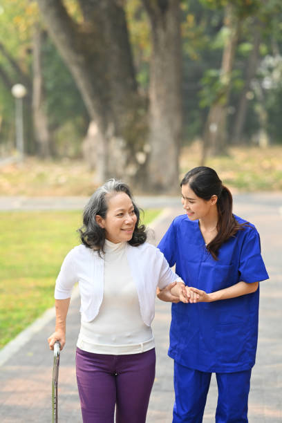 Image of caring female caregiver talking, supporting, helping elderly woman while walking in outdoor. Image of caring female caregiver talking, supporting, helping elderly woman while walking in outdoor. walking aide stock pictures, royalty-free photos & images