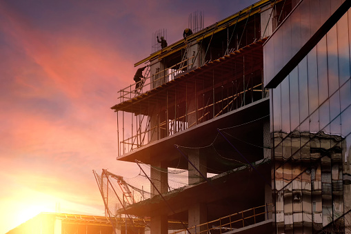 Workers make strapping reinforcement for pouring concrete. Construction of a new residential building against the backdrop of a beautiful sunset sky.