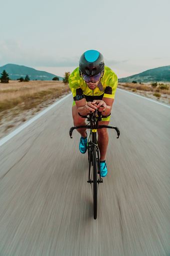 Full length portrait of an active triathlete in sportswear and with a protective helmet riding a bicycle. Selective focus.
