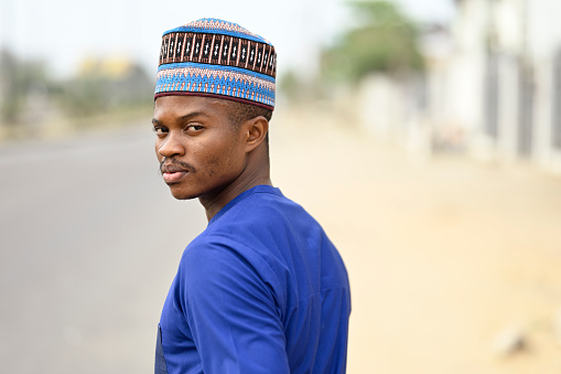 A traditional businessman from the African clan wearing blue attire and his cap to match, Outdoor on the street, standing by the Roadside and copy space.