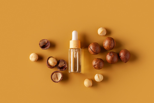 Macadamia oil and nuts on a yellow background. Copy space.