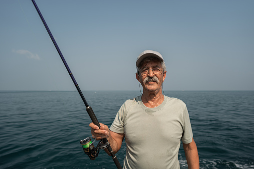 Portrait of a contented senior fisherman holding a fishing rod near the sea.