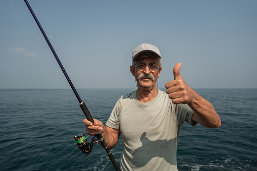 Portrait of a contented senior fisherman showing a thumbs up near the sea.