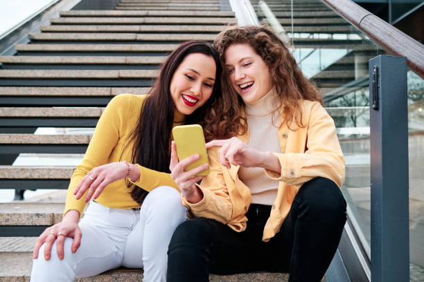 istock Two women smiling and having fun while using mobile phone sitting on stairs outdoors. 1471590991