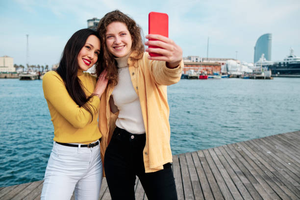 istock Young women smiling while taking selfies with a mobile phone outdoors on the promenade. 1471591038