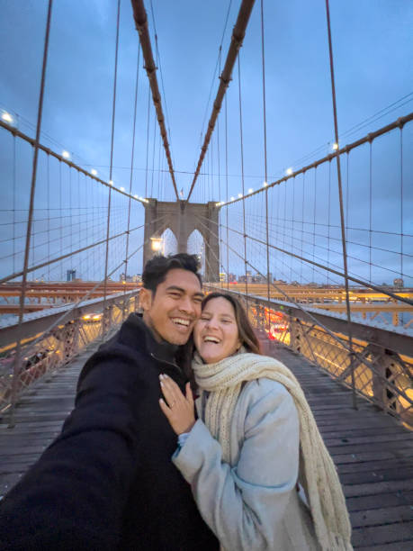 Cheerful couple taking selfie on Brooklyn bridge at dusk