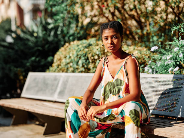 istock Stylish woman looking at camera while sitting on a bench in a park. 1471593120