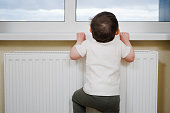Toddler baby climbs to the window near the heating battery. A small child tries to climb on the windowsill. Kid aged one year eight months