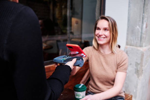 istock Woman smiling while paying with mobile phone at a coffee shop. 1471593598
