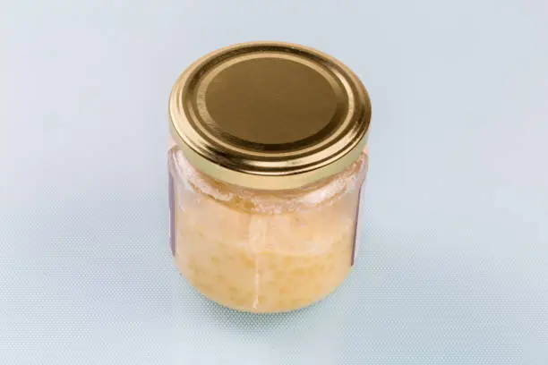 Raw solid cocoa butter in the small glass jar with closed lid on a blue surface