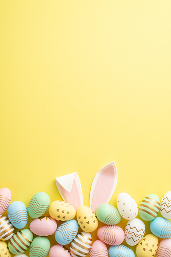 Concepto de celebración de Pascua. Vista superior foto vertical de coloridos huevos de pascua y orejas de conejo de pascua sobre fondo amarillo aislado con espacio vacío photo