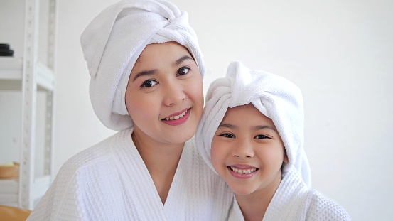 Smiling Asian mother and daughter wearing towels on head after shower and looking at camera. Bathtime concept