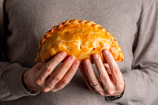 Man hands holding cornish pasty, meat turnover or pie, with filling, beef, carrot, and potato, or empanada.