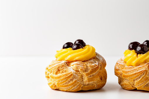 Italian dessert Zeppole di San Giuseppe, zeppola - baked puffs made from choux pastry, filled and decorated with custard cream and cherry. Close-up.