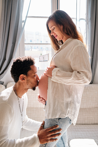 Man kissing his pregnant wife belly at home. Relationship and pregnancy concept.