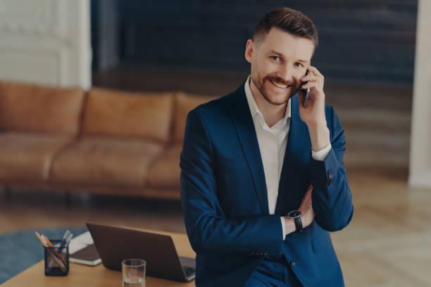 istock Smiling male entrepreneur talking on mobile phone while leaning on office desk 1471598588