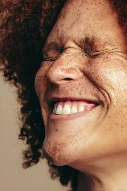Young man with glowing, freckled skin and ginger hair smiles in a studio. Happy and youthful man celebrating his unique beauty features with self-love and self-assurance.
