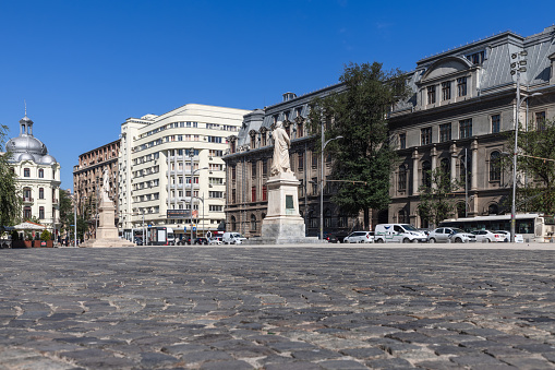 Bucharest - Romania, July 15, 2022. Cobbled University Square and boulevard Regina Elisabeta, view of Bucharest University Faculty of History and monuments statues of Spiru Haret and Gheorghe Lazar