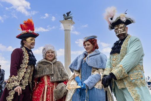 Venice - Italy. February 5, 2023: A group of participants in original costumes of the Venice Carnival on the embankment against the background of the Column of San Marco
