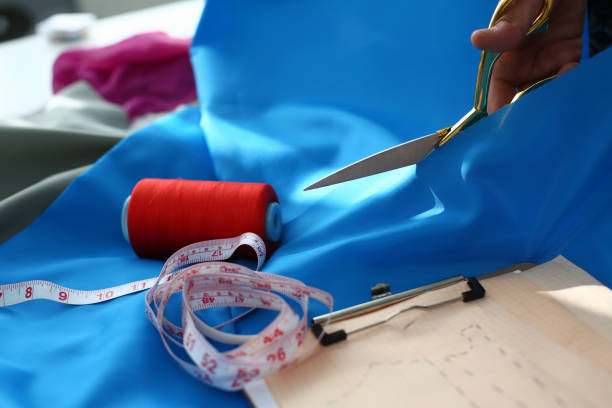 istock Tailor cuts piece of blue fabric at table in fashion studio 1471605131