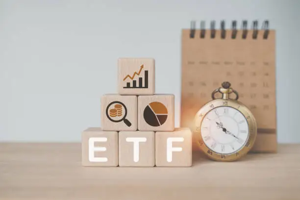 Photo of wooden cube with bitcoin icon standing with ETF text , Exchange Traded Fund, with blurred vintage and calendar. for business finance conceptual