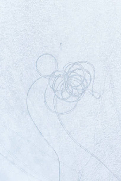 Aerial view of ice and snow on a lake with vehicle tracks in circles and a lone skier.