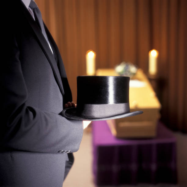 istock Undertaker standing in front of a coffin with a top hat in his hand 1471606383