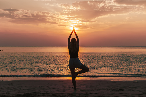Woman practicing yoga on a beach during sunset