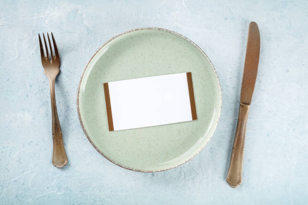 istock Dinner invitation. A card on a green plate, with a fork and a knife, top shot 1471608985