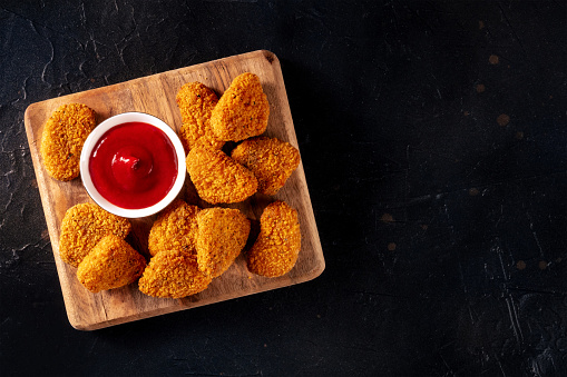 Chicken nuggets with ketchup on a dark background, shot from the top. A crispy meat snack at a restaurant, a fast food dish, with copy space