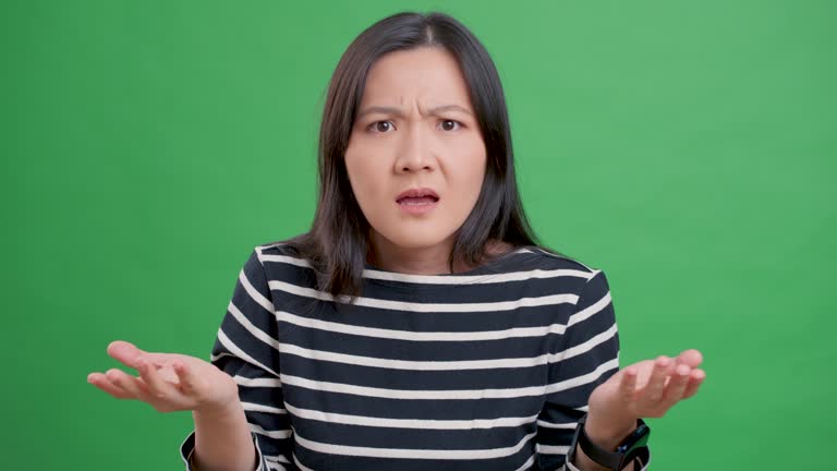 Asian woman feel confused standing isolated over green background.