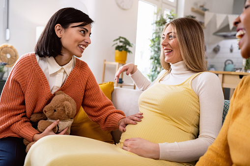 Caucasian woman touching the pregnant belly of her friend, during her baby shower