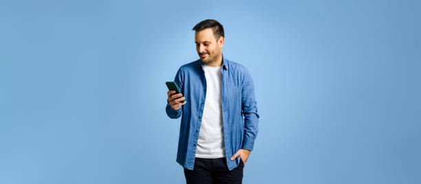 Man with hand in pocket using smart phone on blue background