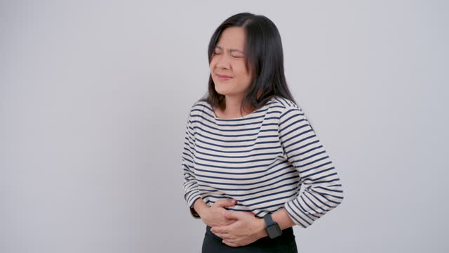 Asian woman suffering from stomach ache standing isolated on white background.