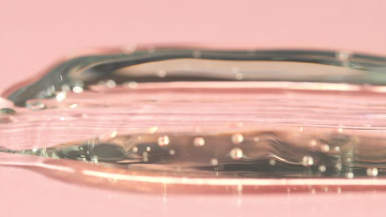 A sample of a transparent peptide, hyaluronic acid on a pink background. Close-up of liquid cosmetic texture.