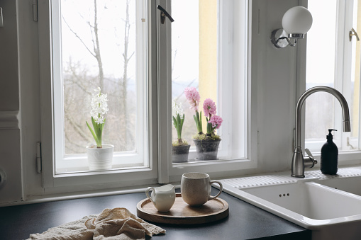 Horizontal image of modern kitchen detail. Showing a kitchen sink and faucet with water running from the faucet, and potted herbs behind on window sill. Space for copy.