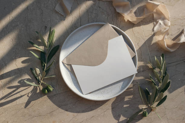 istock Summer branding, wedding stationery. Blank greeting card, envelope mock up on ceramic plate in sunlight. Beige marble background. Olive tree branches, fruit, ribbon. Long shadows. Flat lay, top view. 1471618030