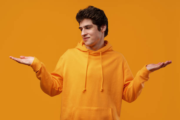 young man standing over yellow background clueless and confused with open arms - blank expression head and shoulders horizontal studio shot imagens e fotografias de stock