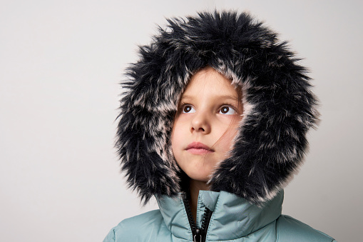 Cute girl wearing winter jacket, white background with copy space. Child girl wear winter coat with fur hood, close-up
