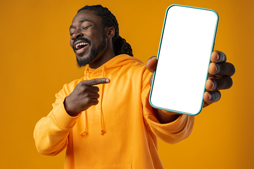Hombre africano sonriente señalando un teléfono celular con pantalla en blanco con espacio de copia photo