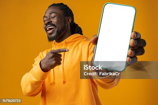 istock Smiling african man pointing at cellphone with blank screen with copy space 1471620723